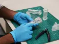 Hands in blue gloves assemble a 3D printed medical device prototype, showcasing innovation in healthcare technology.