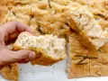 Mano rompiendo un trozo de focaccia casera con romero y sal gruesa. ¡Una delicia de esta focaccia receta!