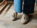 Beżowe mokasyny z frędzlami na drewnianej podłodze. Urocze stupki w casualowym stylu.