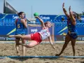 Piłkarka w locie rzuca zieloną piłką podczas meczu beach handball. Rywalki próbują ją zatrzymać.
