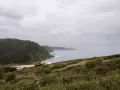 Paisaje costero con acantilados verdes y mar gris. Ideal para senderismo en Villaviciosa, con una playa dorada y una casa blanca.