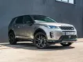 Srebrny Land Rover Discovery Sport z czarnym dachem, zaparkowany przed szarą ścianą.