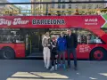 Family posing in front of a red "City Tour Barcelona" bus, ready for an adventure.
