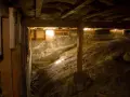 Underneath a house, a crawl space with a dirt floor and concrete walls. A vapor barrier is being installed to protect against moisture.