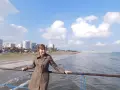 Kobieta na molo, ciesząca się łagodną pogodą w styczniu na Cyprze. W tle plaża i nadmorskie miasto.