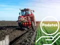 Czerwony traktor orze pole, symbolizując dzierżawę ziemi rolnej i związane z nią podatki.