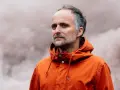 Artur Rojek w pomarańczowej kurtce, otoczony mgłą. Wokalista zespołu Myslovitz.
