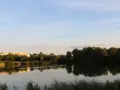 Spiegelglatte Wasserfläche am Wuhletal Wanderweg, reflektiert Bäume und Gebäude. Ein rotes Haus sticht hervor.