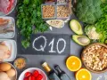 Q10 na tablicy, otoczone produktami bogatymi w koenzym Q10. Warto pamiętać o przeciwwskazaniach przy suplementacji.