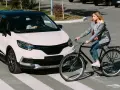 Frau auf Fahrrad kreuzt Straße, Auto hält an. Die Szene erinnert an die **Bremsweg Formel** für Verkehrssicherheit.