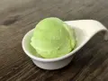 Una bola de helado de manzana verde brillante en una taza blanca sobre una mesa de madera.
