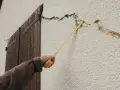 Main d'une personne mesurant des fissures sur un mur extérieur. Quand s'inquiéter des fissures maison ?