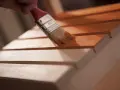 Pędzel nakłada pokost na drewniane listewki, nadając im ciepły, miodowy odcień.