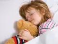 Dziecko śpi wtulone w misia, w głębokim śnie, być może w fazie REM, marząc o przygodach.