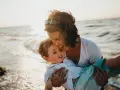 Ciepły moment na plaży, kiedy dziecko daje buziaka mamie. Słońce odbija się w falach.