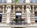 Dwie rzeźby atlantesów podtrzymujące balkon, przykład secesji w sztuce, zdobią fasadę kamienicy.