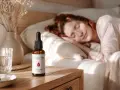 Una mujer duerme plácidamente. A su lado, en la mesita de noche, un frasco de aceite CBD, ideal para saber como tomar aceite de cbd para dormir y disfrutar de un descanso reparador.