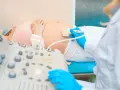 Badanie USG brzucha ciężarnej. Lekarz w niebieskich rękawiczkach wykonuje **test pappa**, sprawdzając stan płodu. Cena badania jest przystępna.