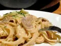 Tagiatelle z grzybami w kremowym sosie, posypane świeżym koperkiem. Widok z bliska na talerz pełen pysznego makaronu.