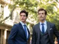Due uomini eleganti in abiti sartoriali, un esempio di stile delle marche abbigliamento uomo famose, passeggiano in una strada alberata.
