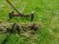 Ein Vertikutierer mit Rädern und Zinken entfernt Moos und Rasenfilz.