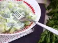 Ensalada cremosa de pepino y yogur con hierbas frescas en un plato blanco con borde rojo.
