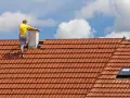 Pracownik na dachu buduje komin systemowy. Sprawdź, jaka jest murowanie komina systemowego cena robocizny.