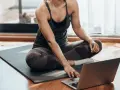 Kobieta w stroju sportowym siedzi na macie, korzystając z laptopa. Czy można ćwiczyć codziennie? Tak, jeśli masz dostęp do inspiracji online!