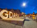 Podświetlany napis "GDAŃSK" na tle nocnej panoramy miasta, zapraszający do odkrywania atrakcji Trójmiasta.