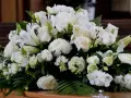 Un arreglo floral blanco sobre un ataúd, con lirios, rosas y otras flores. Estas flores para difuntos simbolizan paz y pureza en el adiós.