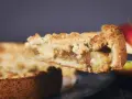 Kawałek najprostszego jabłecznika z kruszonką na widelcu, w tle całe ciasto i jabłka.