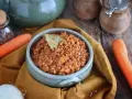 Un invitante ragù di lenticchie, profumato con alloro, pronto per essere gustato. Accanto, carote fresche e cipolla.