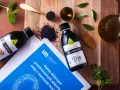 Olej z czarnuszki, bogaty w kwasy omega-3, prezentowany na desce z nasionami i ziołami. Obok butelki z olejem leży dokument z opinią o jego właściwościach.