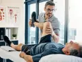 Ein Physiotherapeut dehnt das Bein eines Patienten. Der Patient liegt auf einer Liege, während der Therapeut sein Knie beugt. Wann Physiotherapie? Hier wird geholfen.