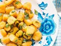 Gnocchi di zucca dorati, conditi con erbe aromatiche e pepe nero, su un piatto decorato con fiori blu.
