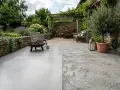 Terrasse avec une finition dalle béton lisse et une autre texturée, mobilier de jardin, brasero et olivier.