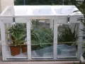 Piccola serra da balcone in legno e plexiglass, ospita diverse piante grasse in vasi di terracotta.