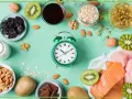 Zielony budzik obok produktów bogatych w tryptofan: łososia, indyka, kiwi, orzechów, migdałów, śliwek, mleka, owsa i czekolady. Zastanawiasz się, po jakim czasie działa tryptofan?