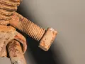Zapieczona śruba, pokryta grubą warstwą rdzy, wygląda jak relikt przeszłości. Jej gwint jest ledwo widoczny pod brązowym nalotem.