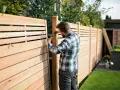 Uomo con trapano realizza una staccionata in legno fai da te, creando un'elegante divisione per il giardino.