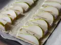 Ciasto francuskie z gruszką i camembert, ułożone rzędami na blasze, gotowe do pieczenia.