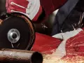 Ręce w czerwonych rękawicach używają szlifierki kątowej, by czym przeciąć metal. Iskry sypią się wokół.