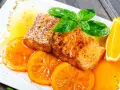 Delicioso salmón a la naranja, servido con rodajas de naranja fresca y hojas de albahaca.