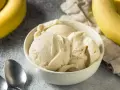 Un cremoso helado de plátano en un tazón blanco, con plátanos amarillos frescos al lado.