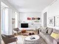 Salón moderno con sofás grises, mesas de centro y arte abstracto. Se aprecia la sutil diferencia entre blanco y blanco roto en paredes y carpintería.