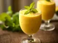 Orzeźwiający mango lassi z mlekiem kokosowym, ozdobiony listkiem mięty. Idealny na upalne dni.