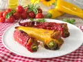 Peperoni cornetti ripieni, rossi e gialli, cotti al forno, su un piatto bianco con pomodorini e basilico.