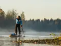 Mann auf Stand Up Paddle, achtet auf die ruhige Wasseroberfläche und die neblige Morgenstimmung.