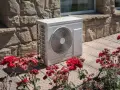 Unità esterna di una pompa di calore aria calda e fredda, posizionata su un patio con rose rosse in fiore.