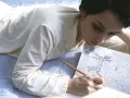 Junge Frau liegt auf dem Bett und schreibt mit Bleistift in ein Notizbuch. Sie ist vertieft in ihr diary entry schreiben.